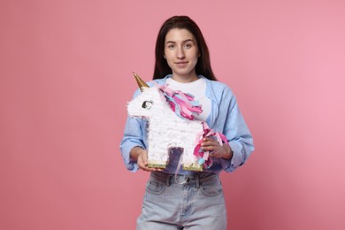 Photo of Woman with unicorn shaped pinata on pink background