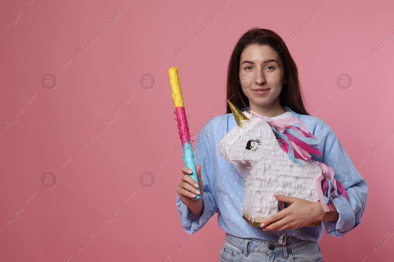 Photo of Woman with unicorn shaped pinata and stick on pink background, space for text