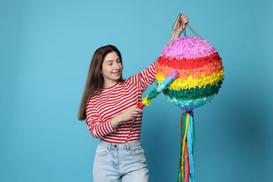 Happy woman with colorful pinata and stick on light blue background