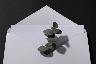 Photo of Paper envelope with letter and eucalyptus branch on black background, above view. Mockup for design