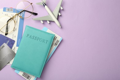 Photo of Passport with tickets, credit cards, glasses and airplane model on lilac background, flat lay. Space for text