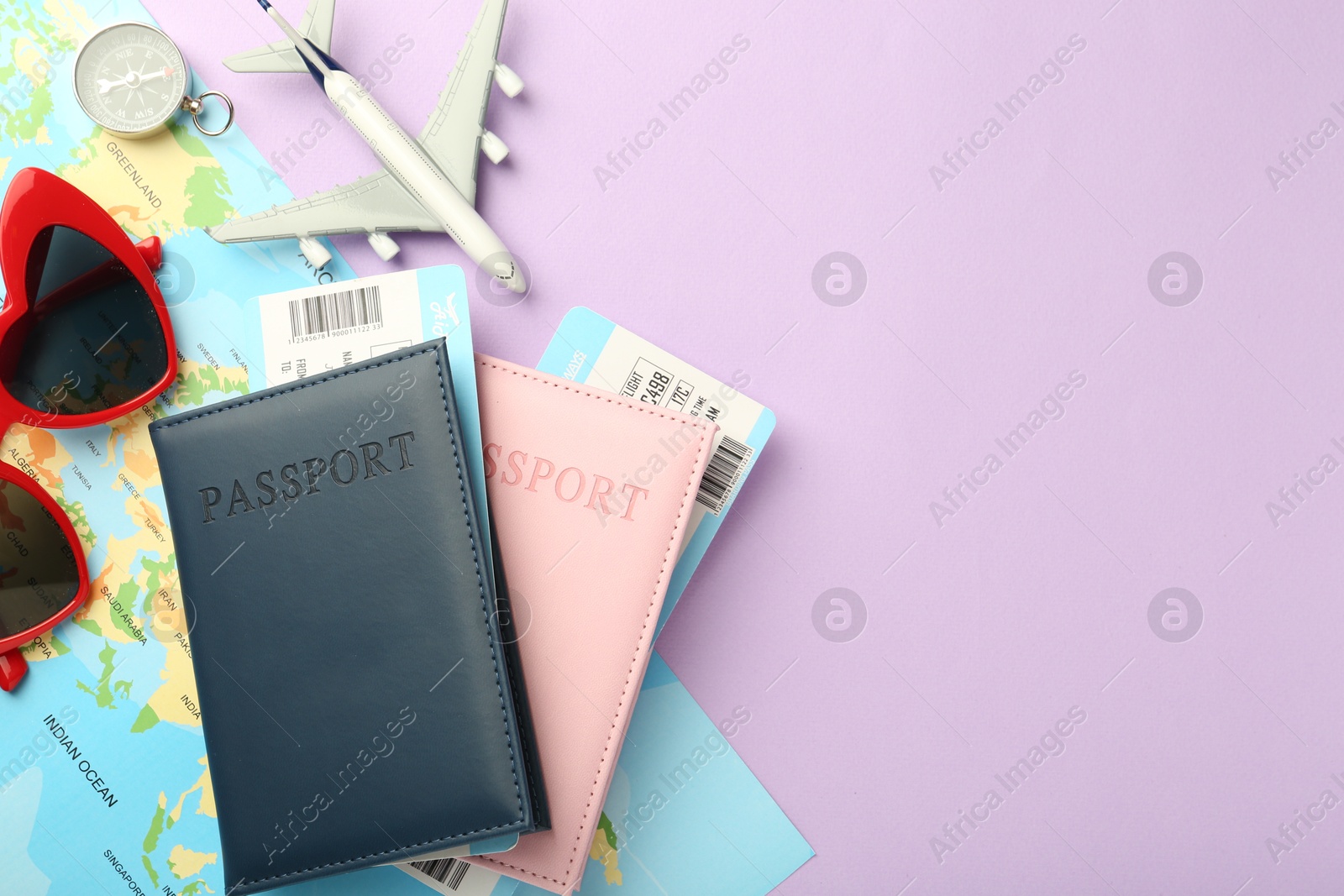 Photo of Passports with tickets, compass, map, sunglasses and airplane model on lilac background, flat lay. Space for text