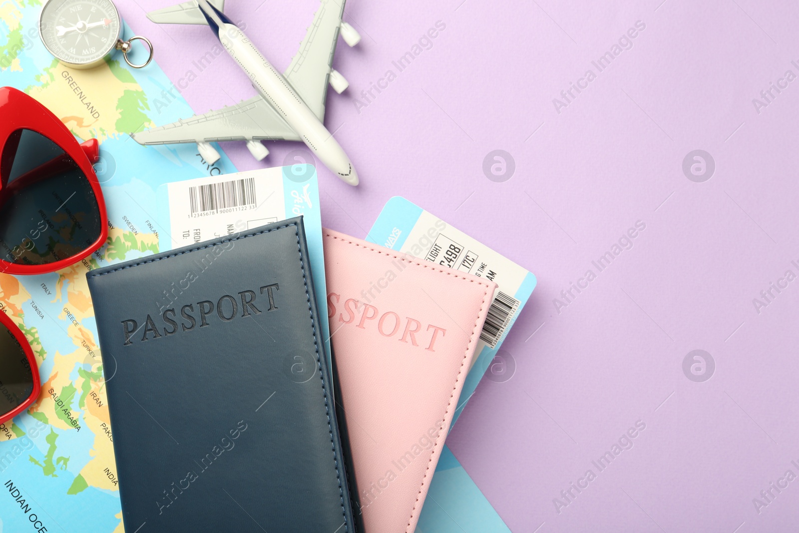 Photo of Passports with tickets, compass, map, sunglasses and airplane model on lilac background, flat lay. Space for text