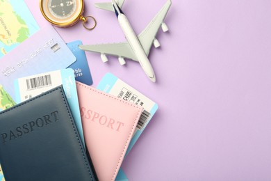 Photo of Passports with tickets, compass, map, credit cards and airplane model on lilac background, flat lay. Space for text