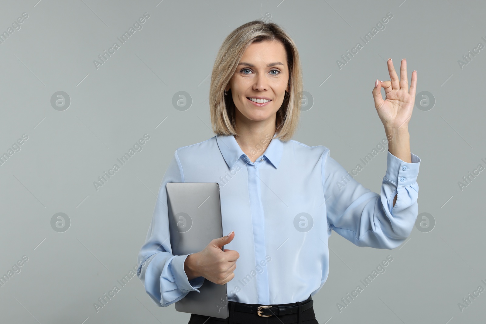 Photo of Smiling businesswoman with laptop showing okay gesture on grey background