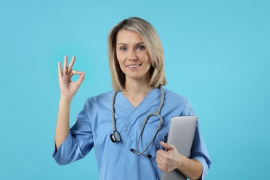 Photo of Doctor with laptop showing okay gesture on light blue background