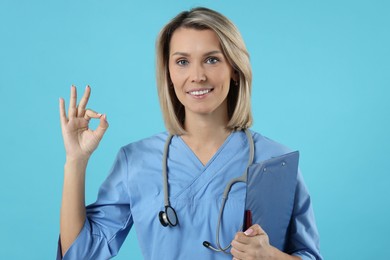 Photo of Doctor with clipboard showing okay gesture on light blue background