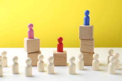 Photo of Competition concept. Human figures on wooden cubes and other ones behind against color background