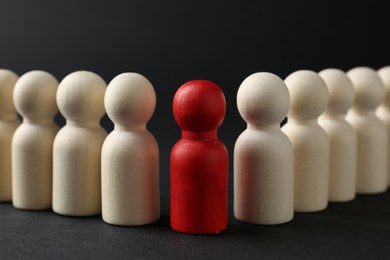 Photo of Competition concept. Red human figure among wooden ones on black background, closeup