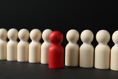 Photo of Competition concept. Red human figure among wooden ones on black background, closeup