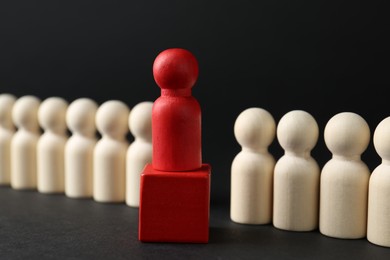 Photo of Competition concept. Human figure on wooden cube and other ones behind against black background, closeup