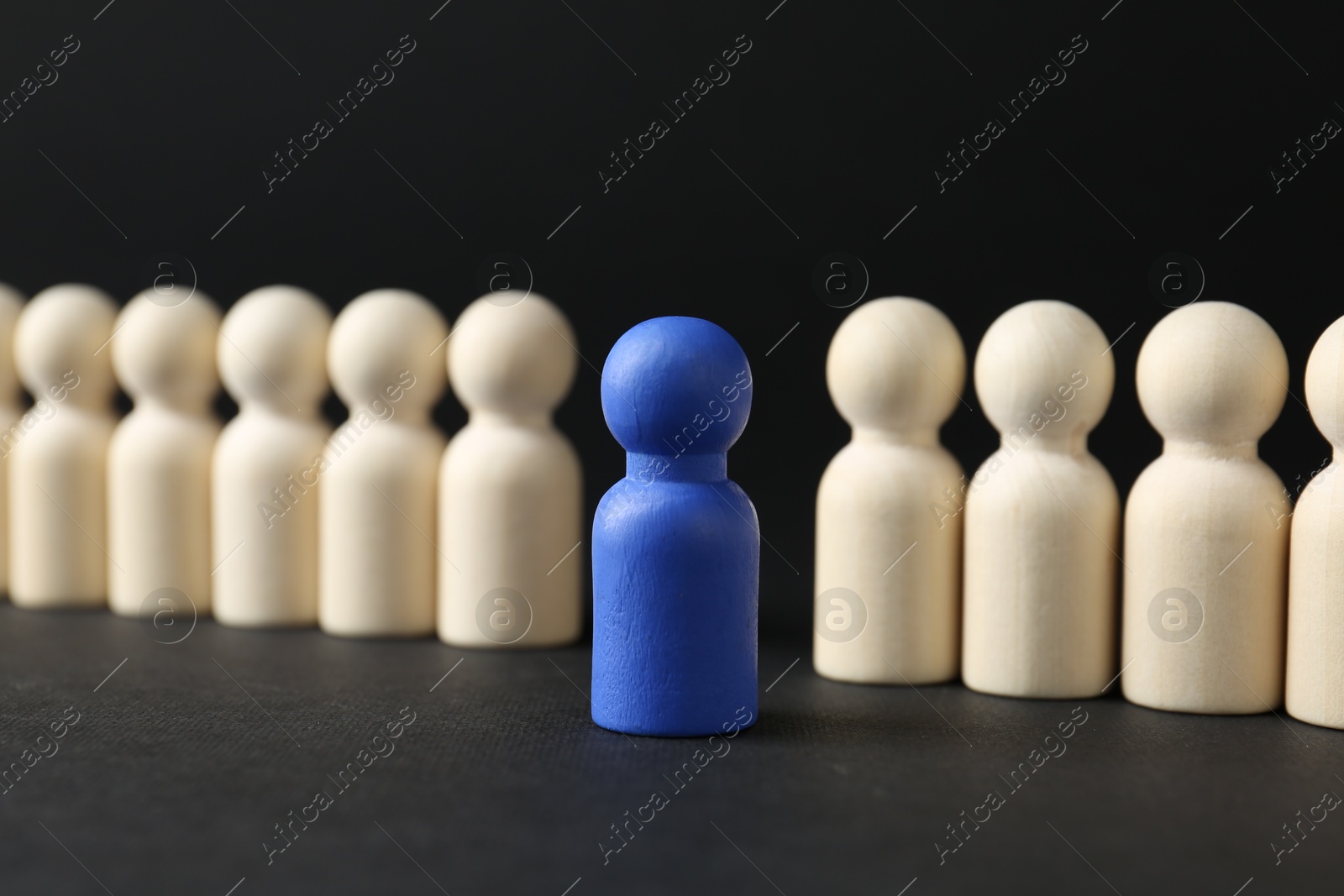 Photo of Competition concept. Blue human figure among wooden ones on black background, closeup