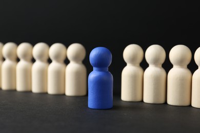 Photo of Competition concept. Blue human figure among wooden ones on black background, closeup