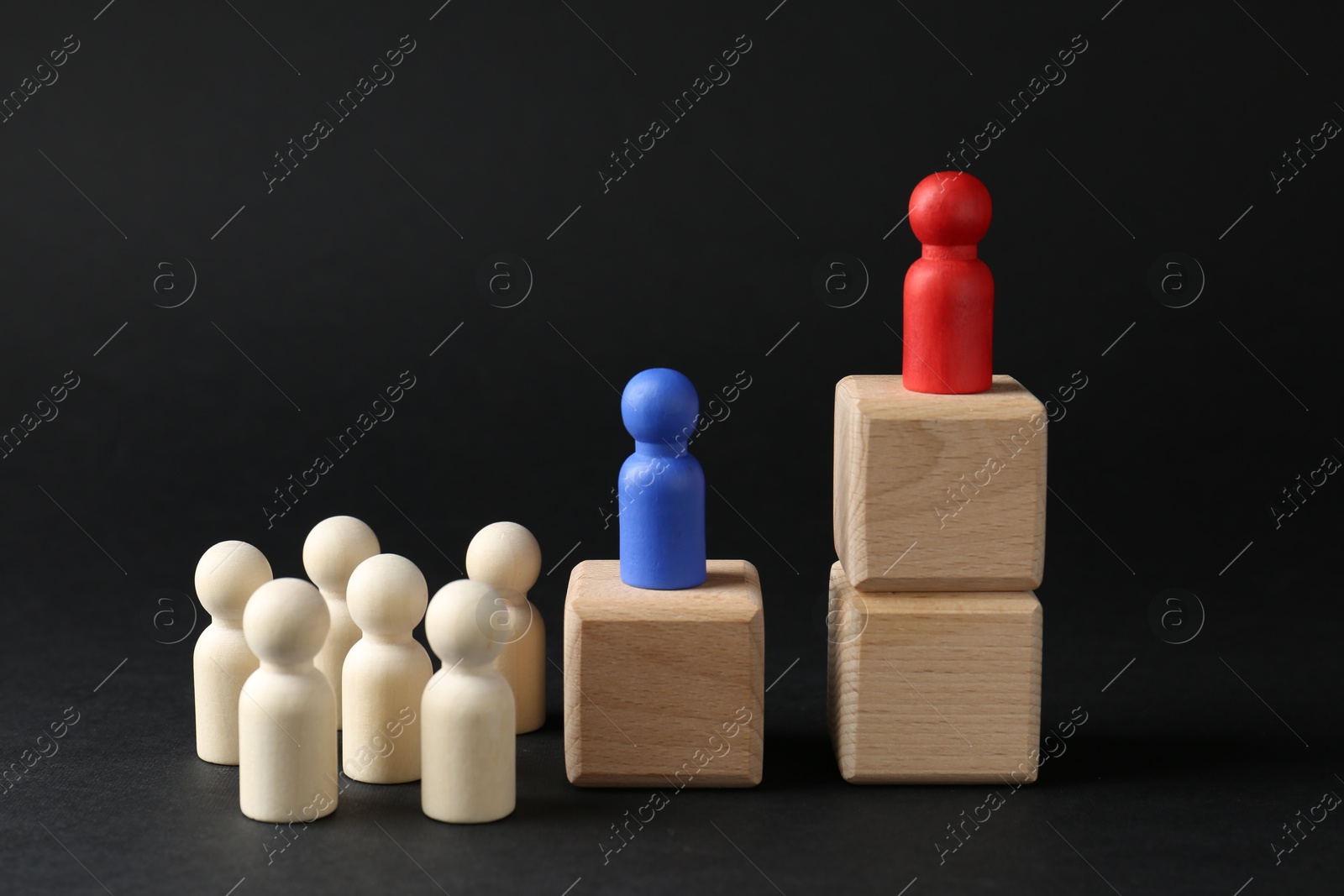 Photo of Competition concept. Human figures on wooden cubes and other ones behind against black background