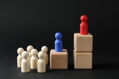 Photo of Competition concept. Human figures on wooden cubes and other ones behind against black background