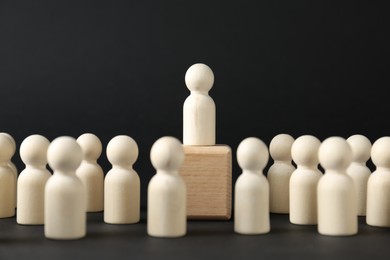 Competition concept. Human figure on wooden cube and other ones behind against black background