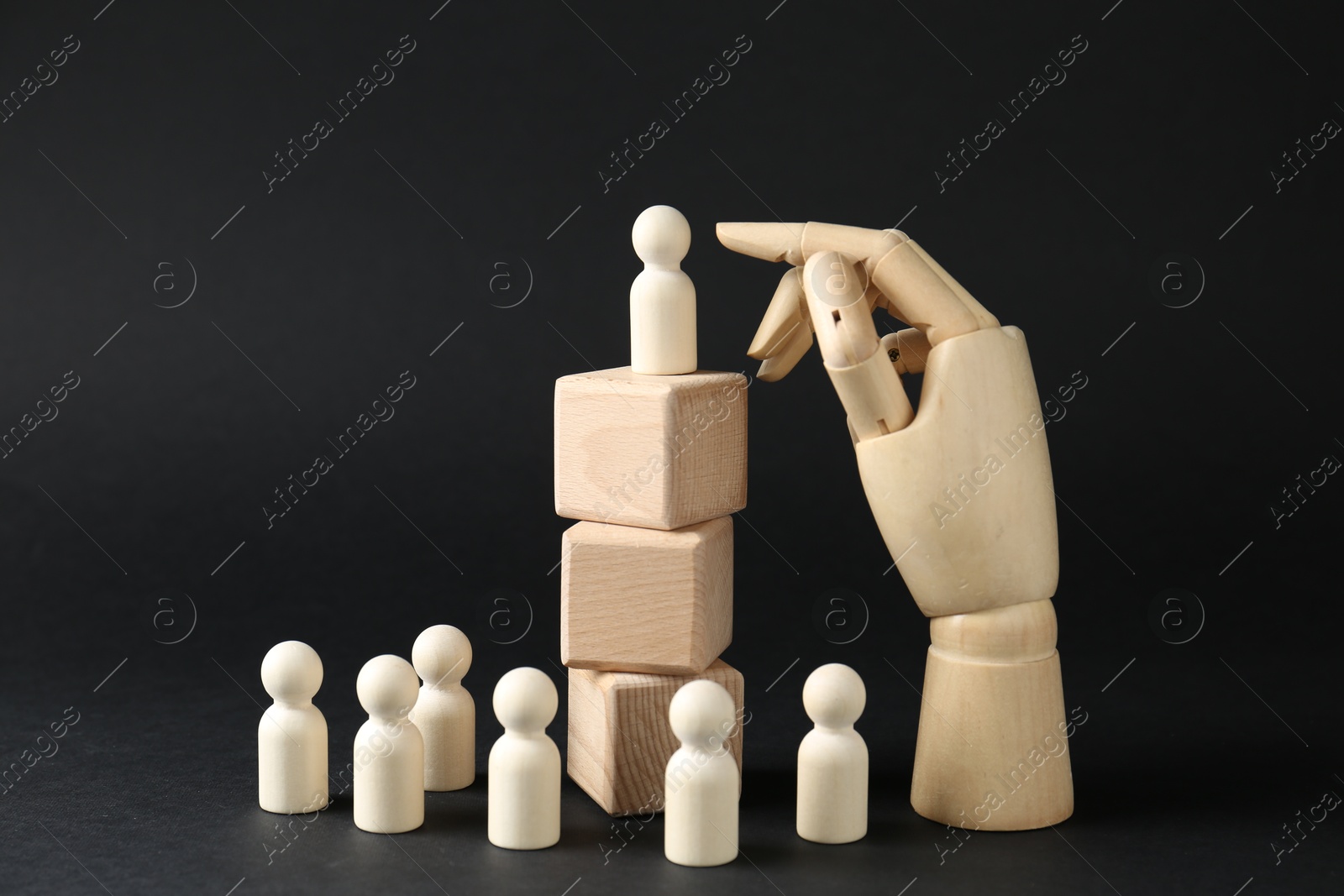 Photo of Competition concept. Human figure on wooden cubes, other ones behind and hand model against black background