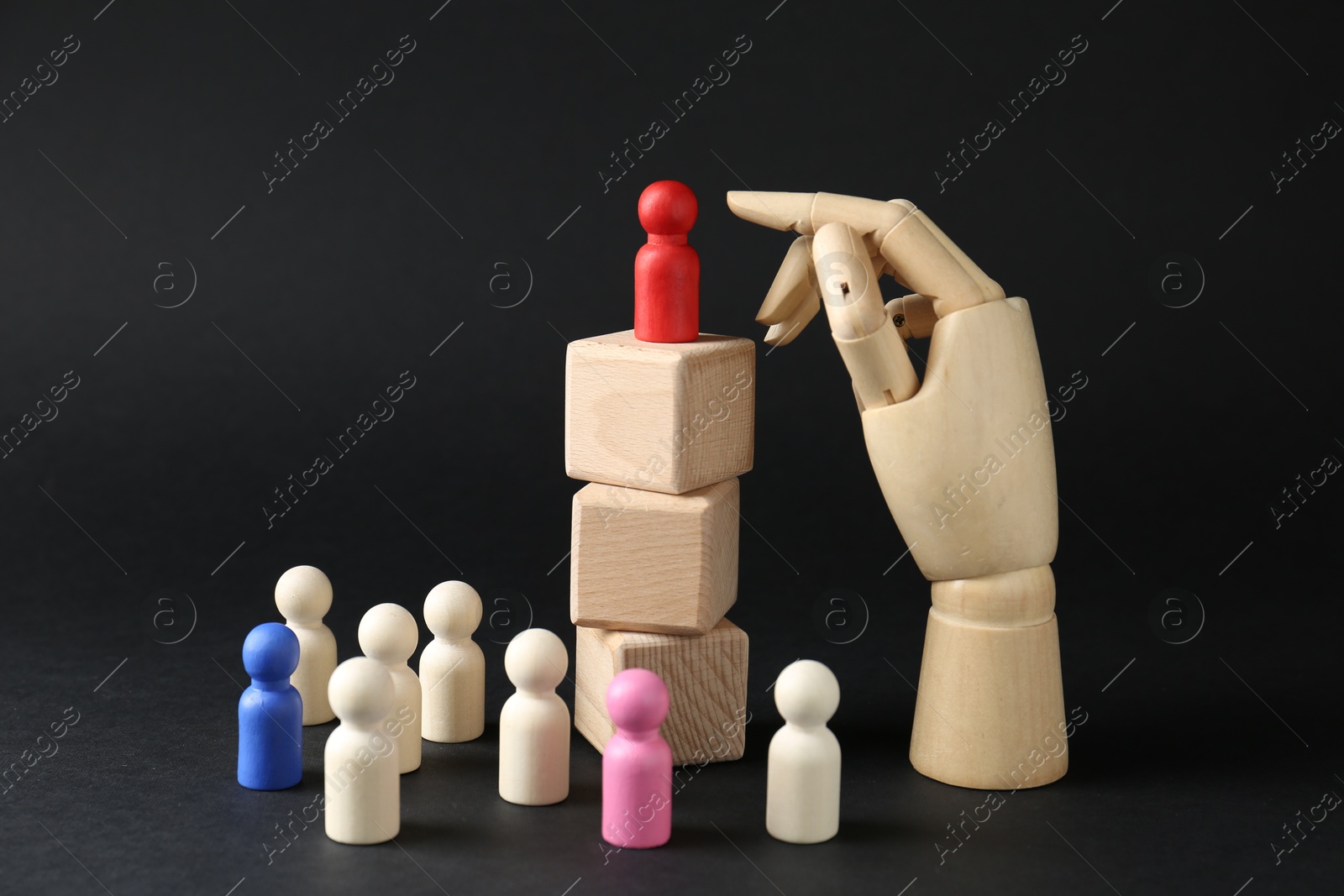 Photo of Competition concept. Human figure on wooden cubes, other ones behind and hand model against black background