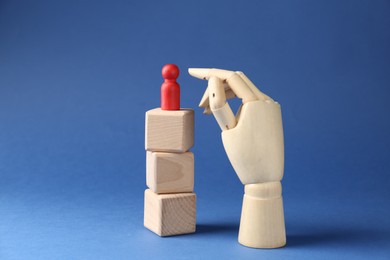 Photo of Competition concept. Human figure on wooden cubes and hand model against blue background