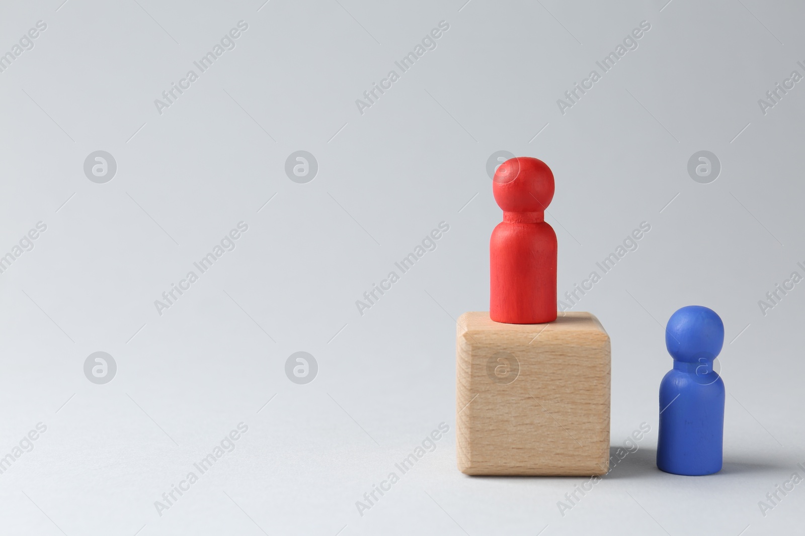 Photo of Competition concept. Human figure on wooden cube and other one behind against light background, space for text