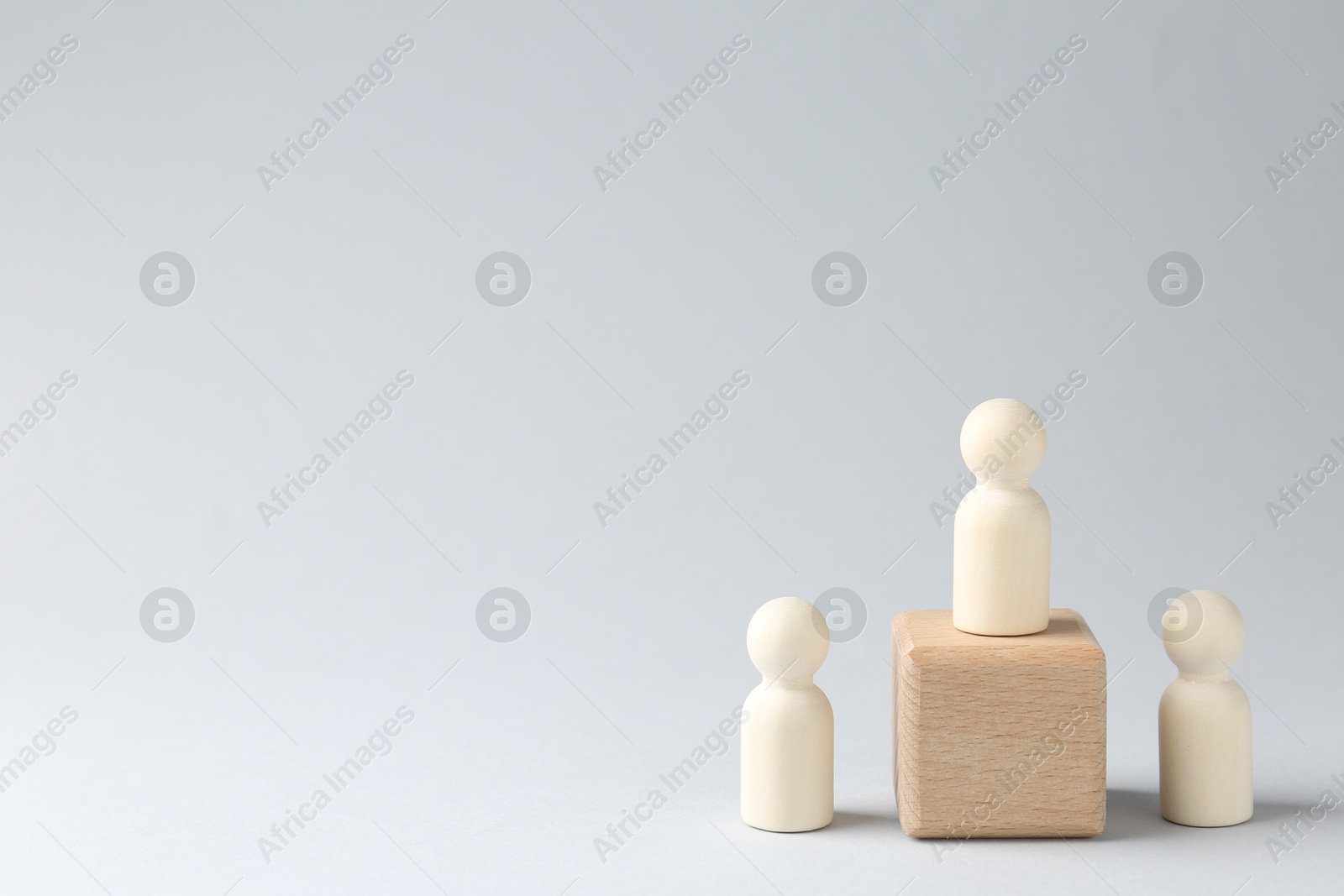 Photo of Competition concept. Human figure on wooden cube and other ones behind against light background, space for text