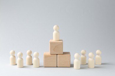 Photo of Competition concept. Human figure on wooden cubes and other ones behind against light background