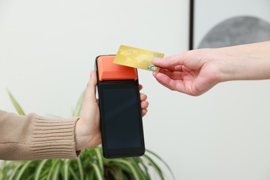 Photo of Woman paying for service with credit card via terminal indoors, closeup