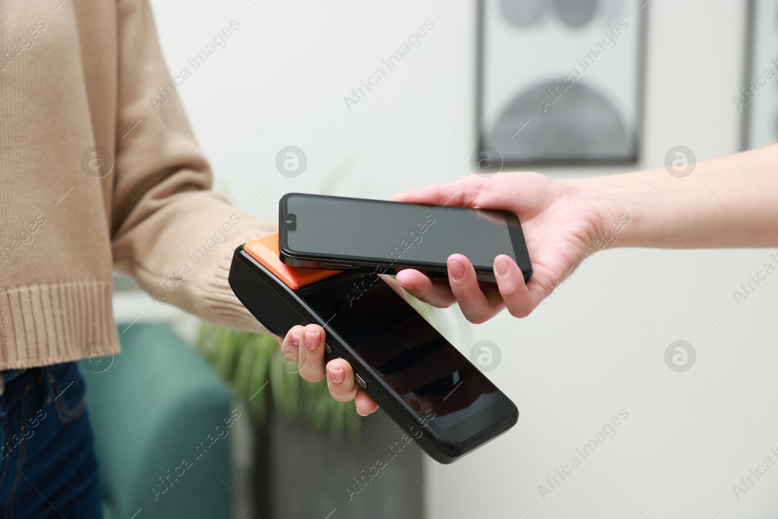 Photo of Woman paying for service with smartphone via terminal indoors, closeup