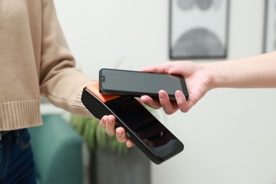 Photo of Woman paying for service with smartphone via terminal indoors, closeup