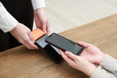 Photo of Woman paying for service with smartphone via terminal at wooden table indoors, closeup