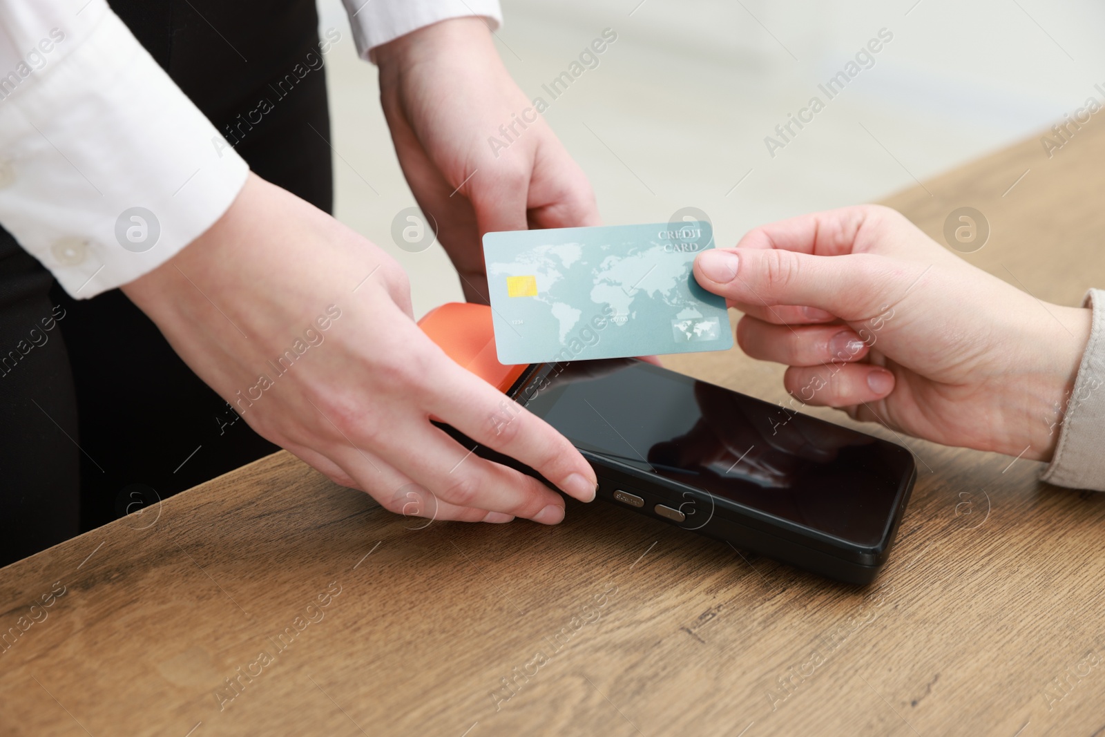 Photo of Woman paying for service with credit card via terminal at wooden table indoors, closeup