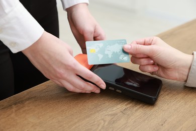 Photo of Woman paying for service with credit card via terminal at wooden table indoors, closeup