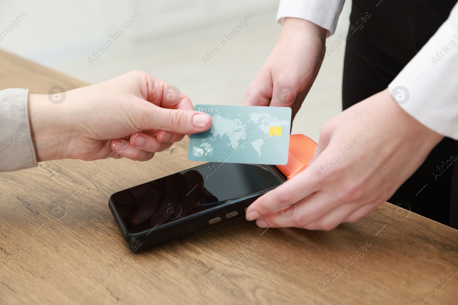 Photo of Woman paying for service with credit card via terminal at wooden table indoors, closeup