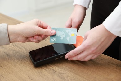 Photo of Woman paying for service with credit card via terminal at wooden table indoors, closeup