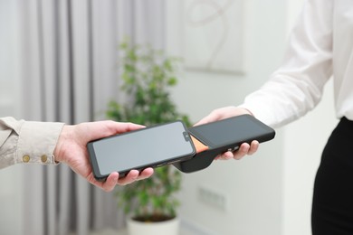 Photo of Woman paying for service with smartphone via terminal indoors, closeup