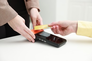 Photo of Woman paying for service with credit card via terminal at white table indoors, closeup