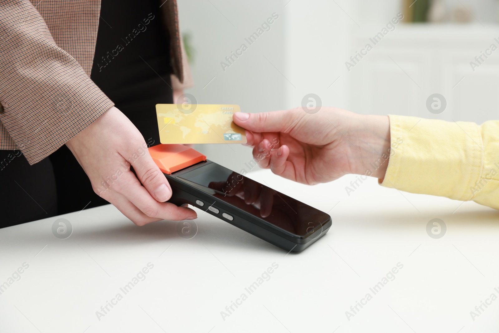 Photo of Woman paying for service with credit card via terminal at white table indoors, closeup