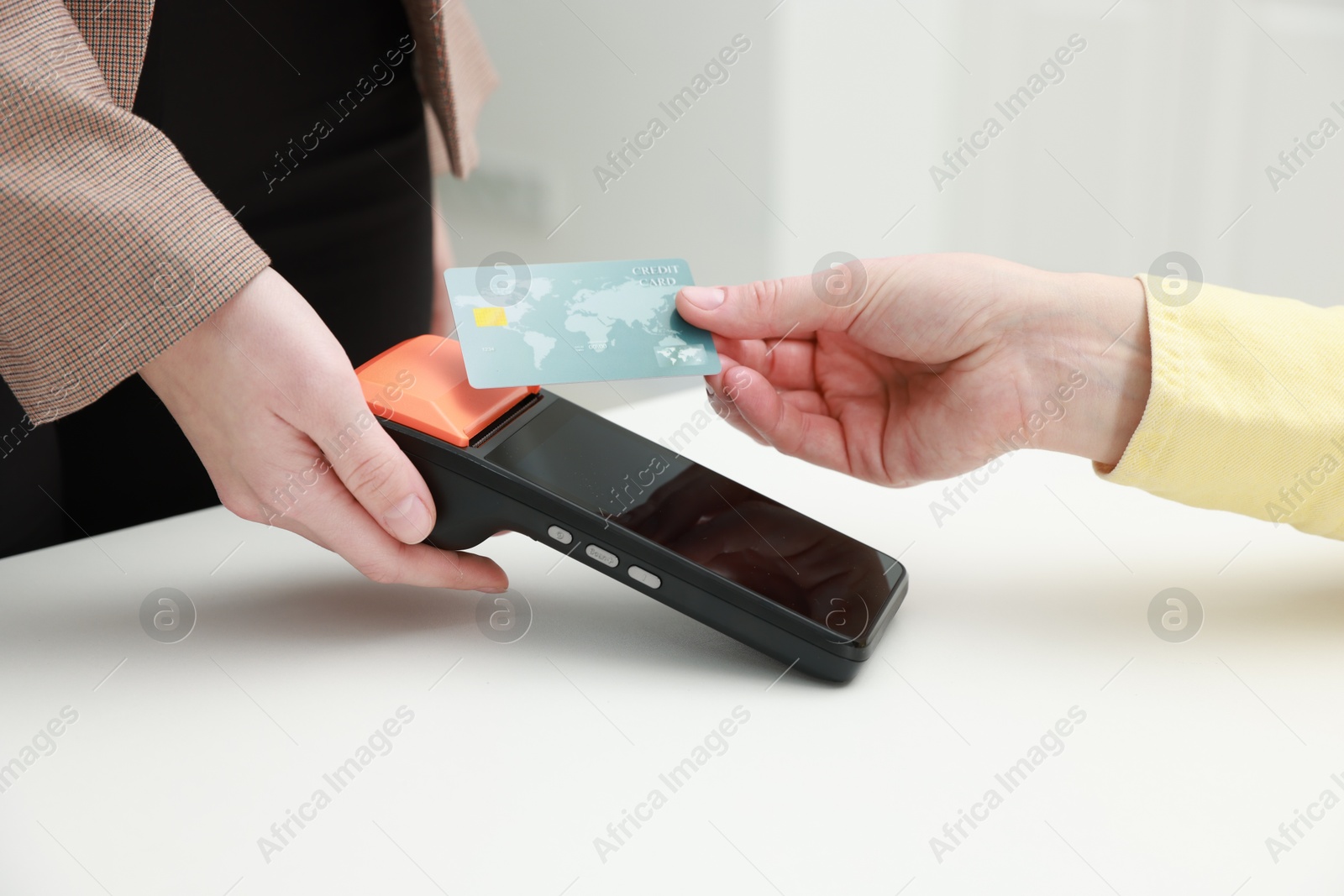 Photo of Woman paying for service with credit card via terminal at white table indoors, closeup