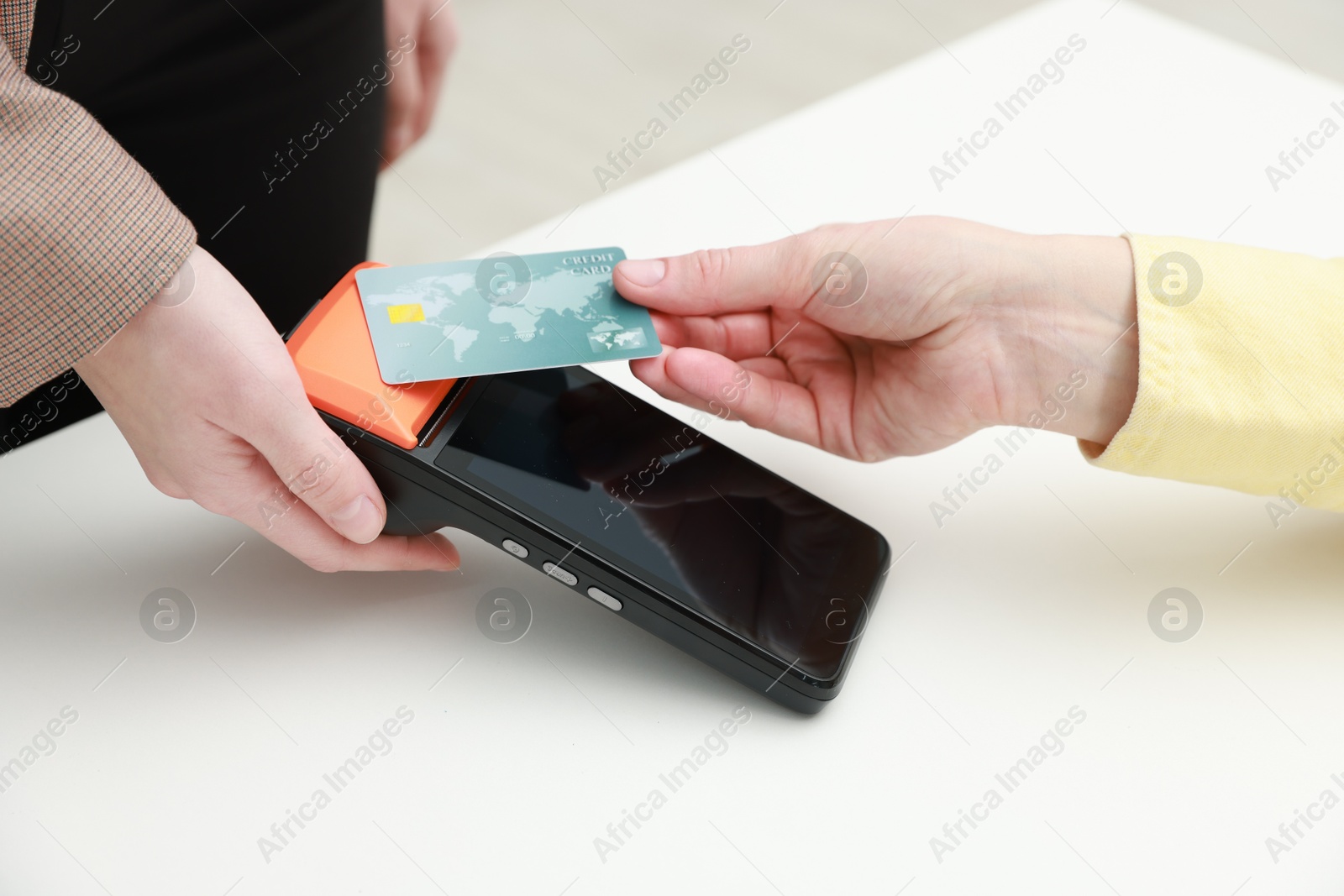 Photo of Woman paying for service with credit card via terminal at white table indoors, closeup