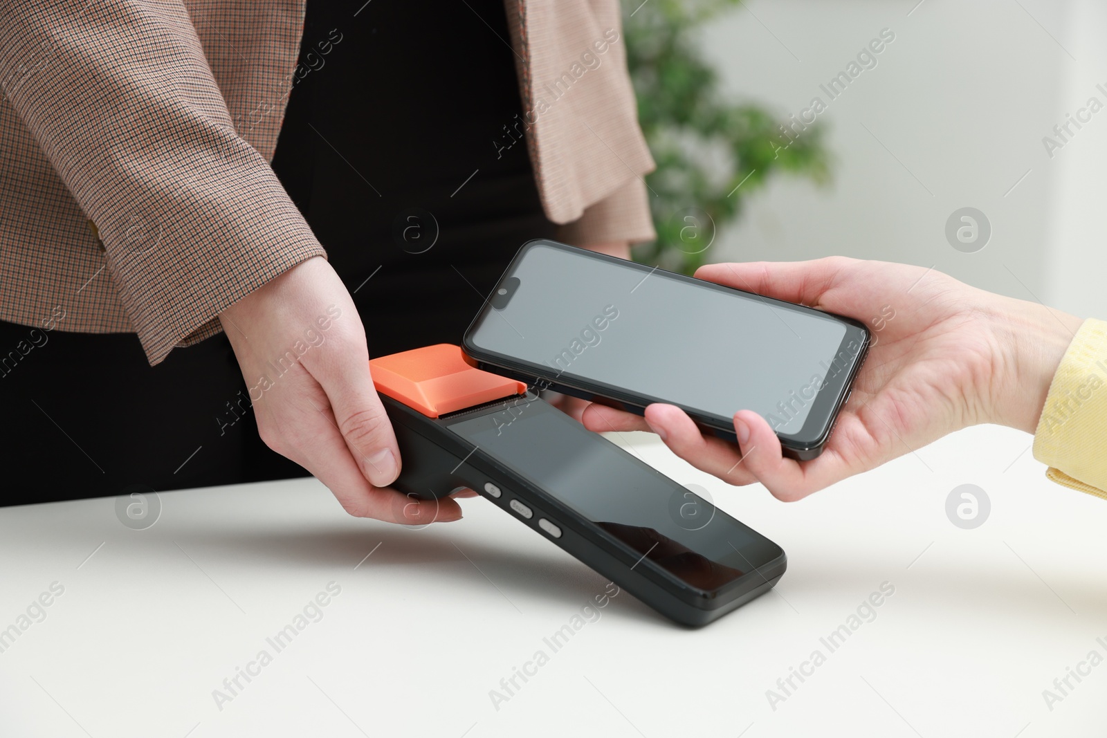 Photo of Woman paying for service with smartphone via terminal at white table indoors, closeup