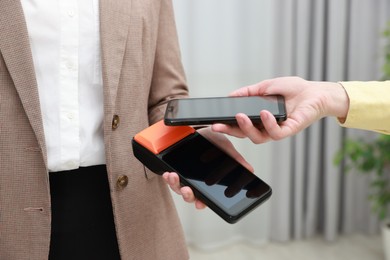 Photo of Woman paying for service with smartphone via terminal indoors, closeup