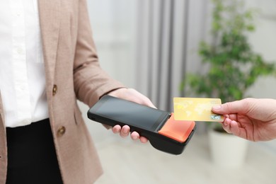 Photo of Woman paying for service with credit card via terminal indoors, closeup