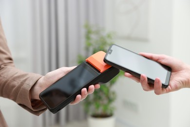 Photo of Woman paying for service with smartphone via terminal indoors, closeup