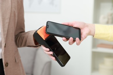 Photo of Woman paying for service with smartphone via terminal indoors, closeup