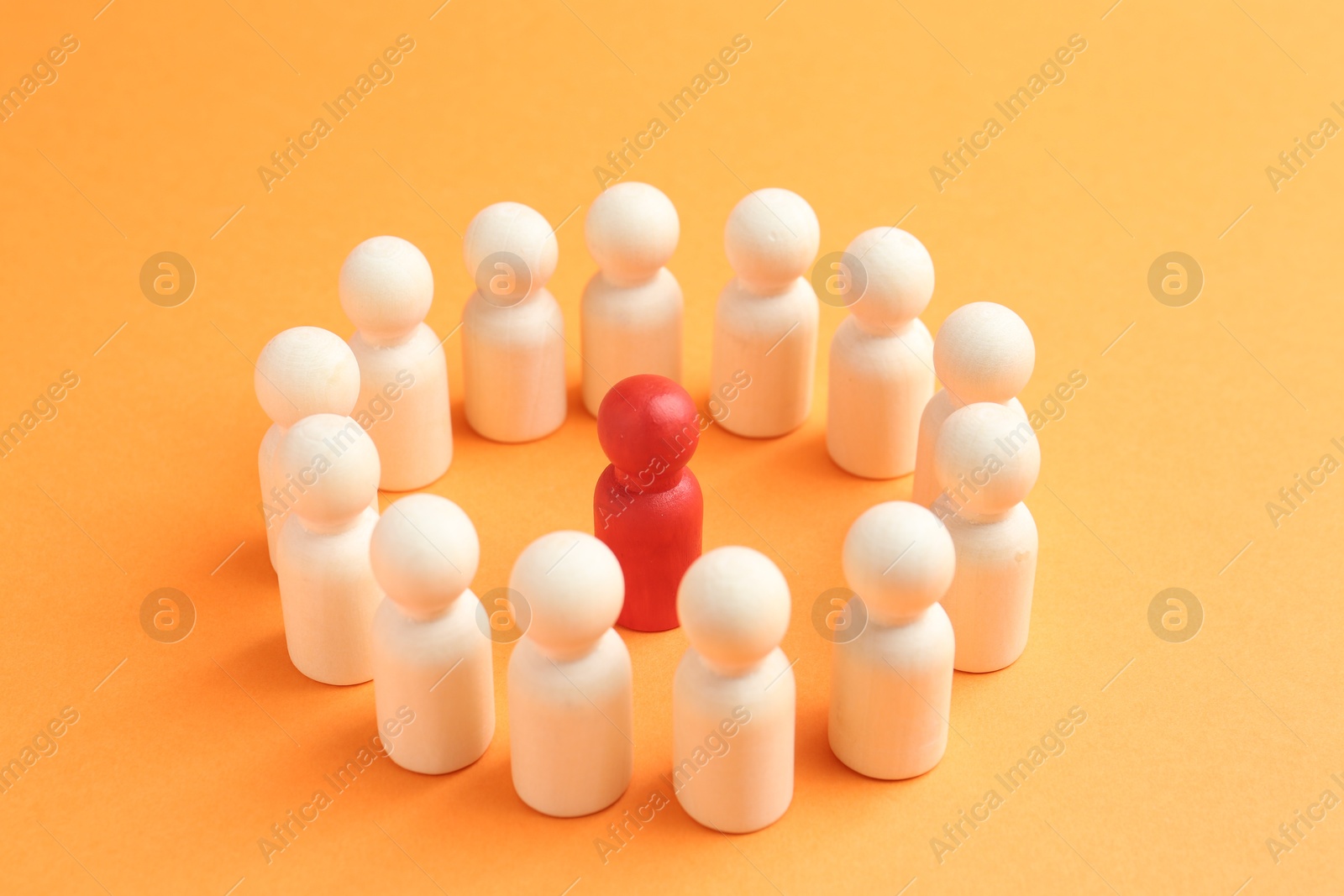 Photo of Red human figure among white ones on orange background, closeup. Competition concept