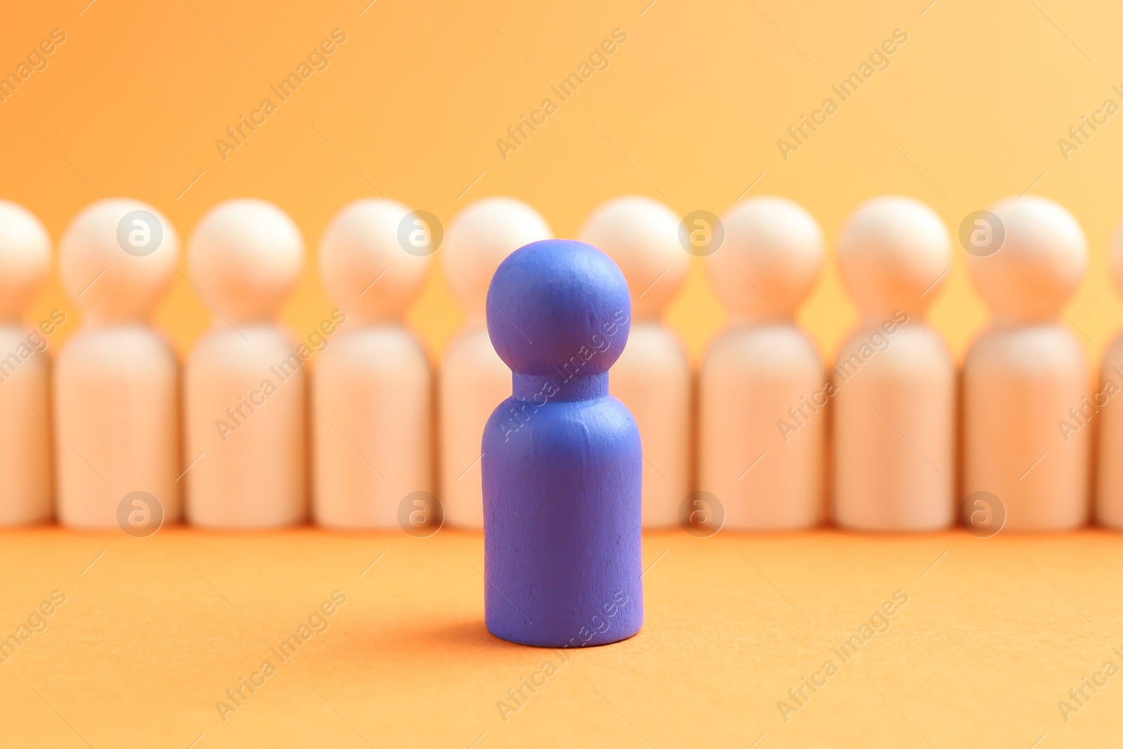 Photo of Blue human figure in front of wooden ones against orange background, closeup. Competition concept