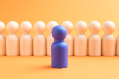 Photo of Blue human figure in front of wooden ones against orange background, closeup. Competition concept