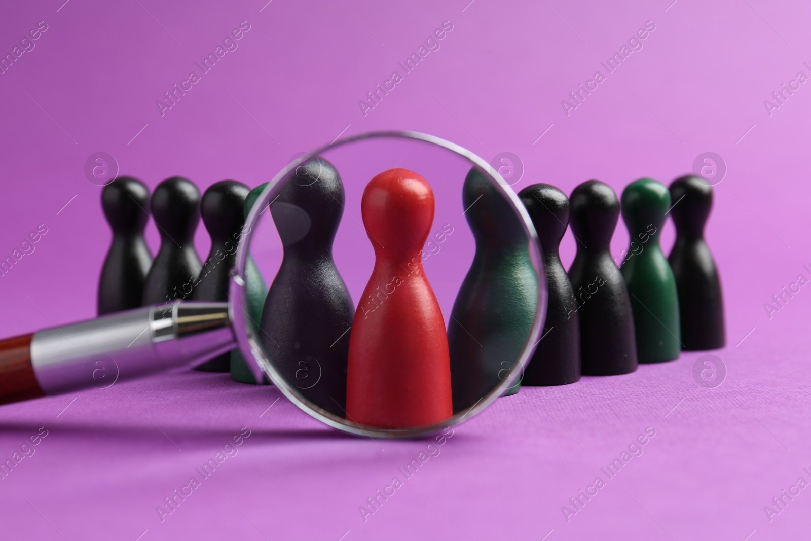 Photo of Looking at human figures through magnifying glass against violet background, closeup. Competition concept