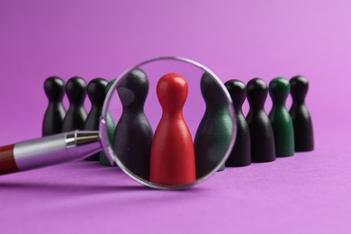 Photo of Looking at human figures through magnifying glass against violet background, closeup. Competition concept