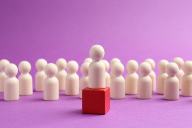 Photo of Human figure on red cube in front of other wooden ones against violet background. Competition concept